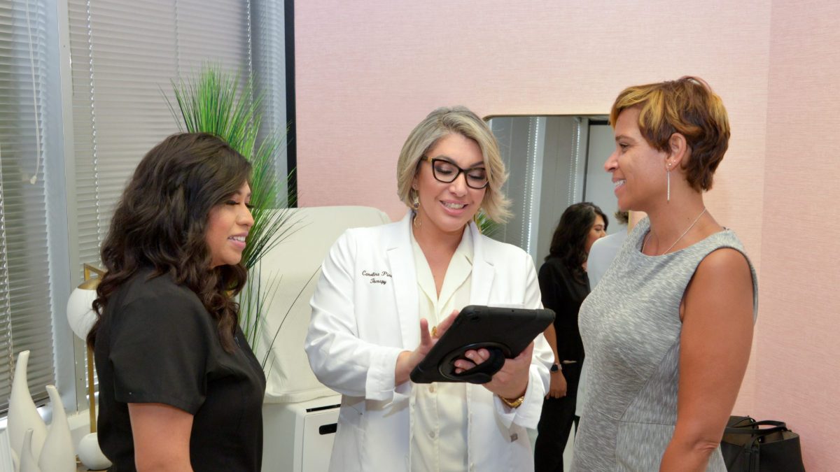 Discussing swelling after a tummy tuck at a Houston post-surgical consultation Carolina Pintos reviewing a recovery plan on a tablet with a post-surgical client in her Houston clinic